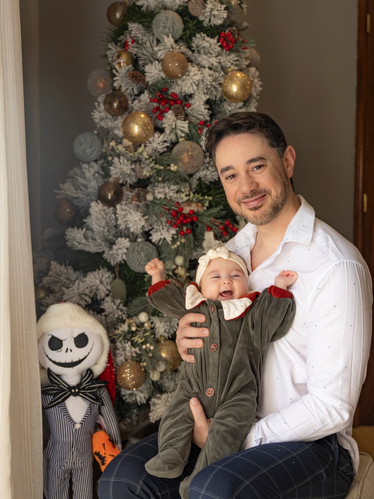 Pai com a bebé sorridente ao colo junto à árvore de Natal