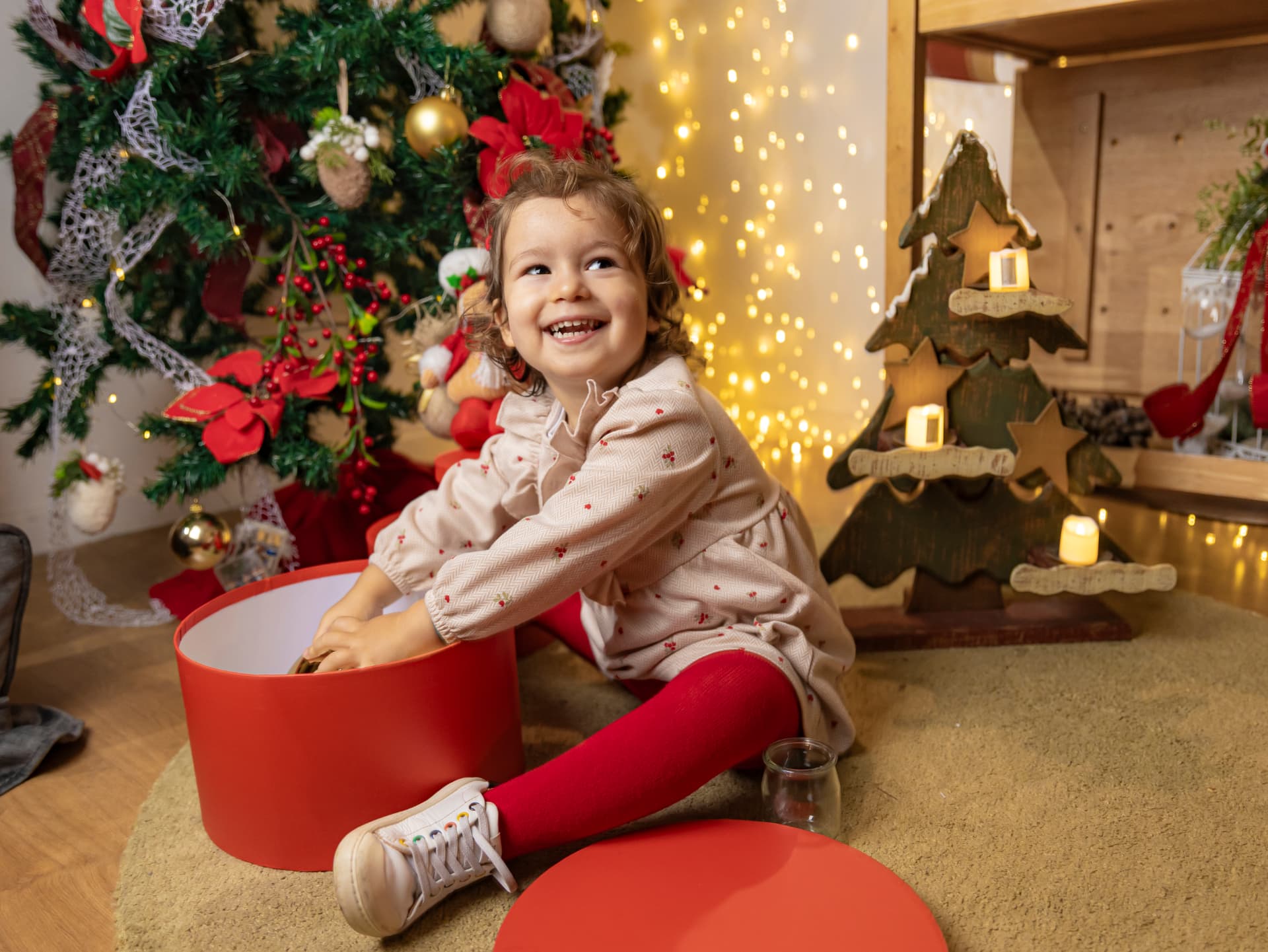 Menina a brincar com uma caixa vermelha junto à árvore de Natal
