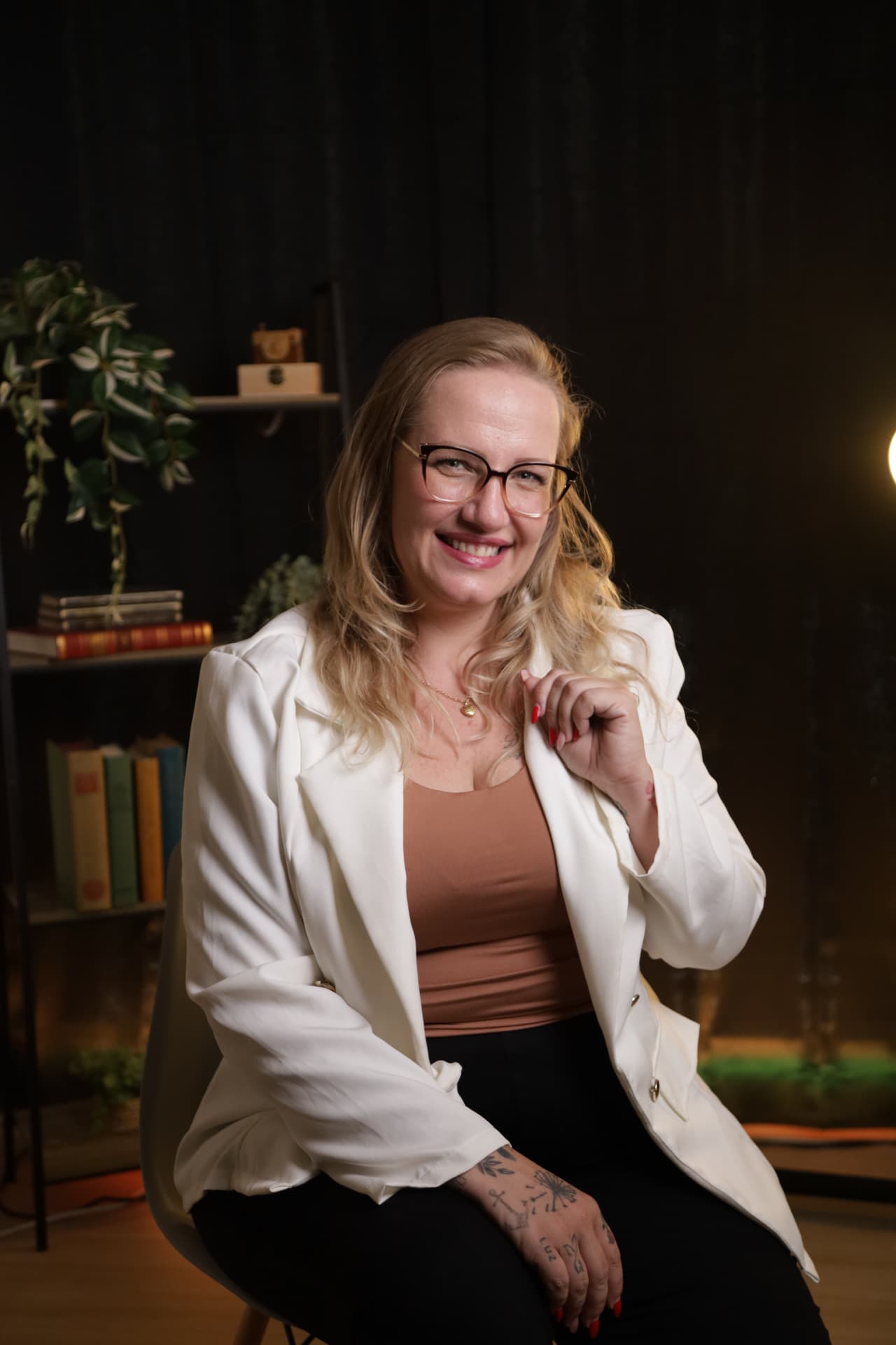 Retrato de Luciana Natália sentada, de blazer branco, num estúdio com estantes de livros